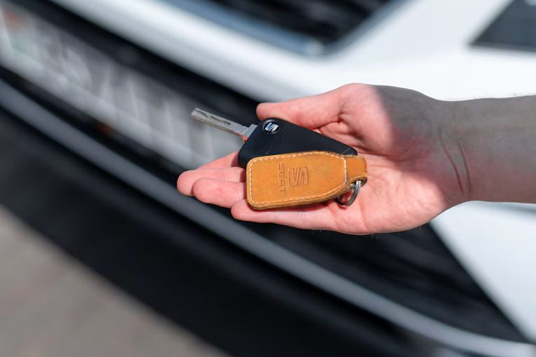 Hand mit Autoschlüssel vor einem Auto